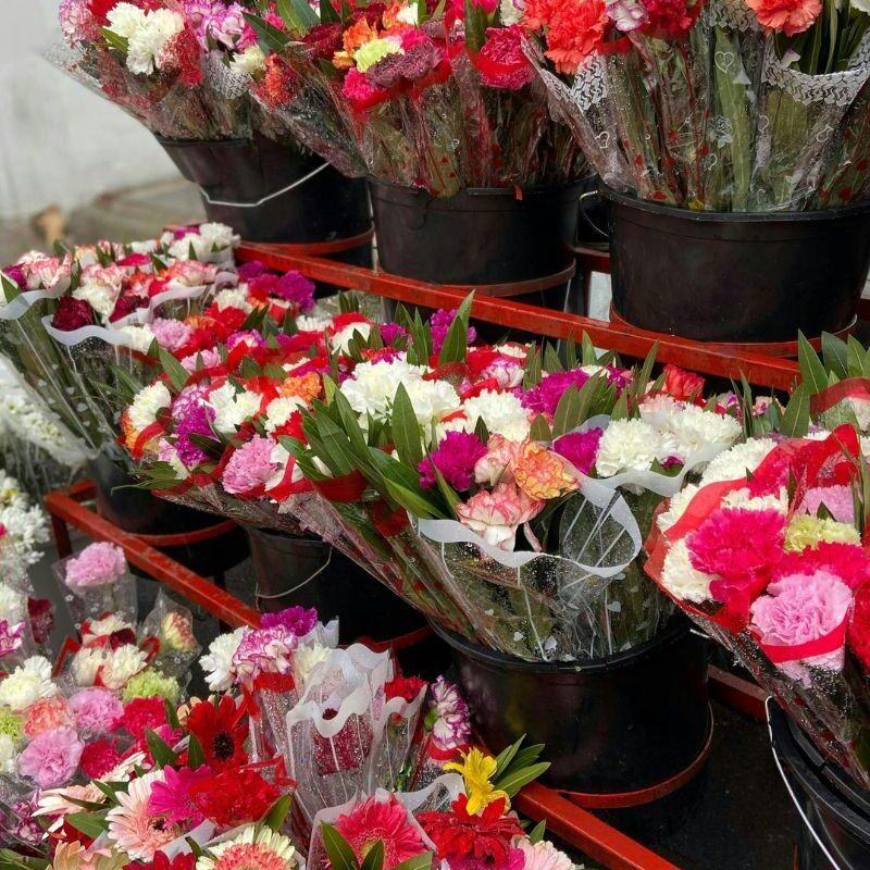 Seaux de fleuriste présentant des bouquets d'œillets rouges, roses et blancs prêts pour la vente au détail.